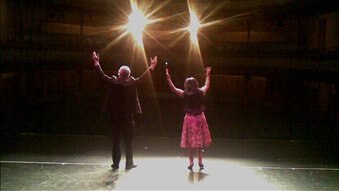 Two people stand on stage with their arms upraised.