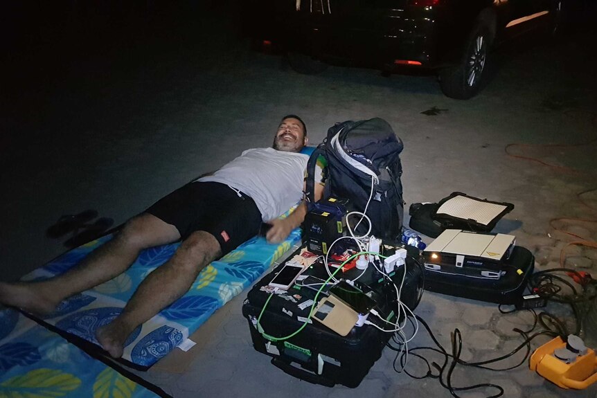 Hemingway lying on mattress on ground surrounded by camera equipment.