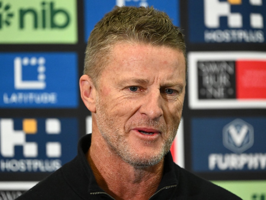 An AFL coach smiles as he speaks to the media after resigning from his post.