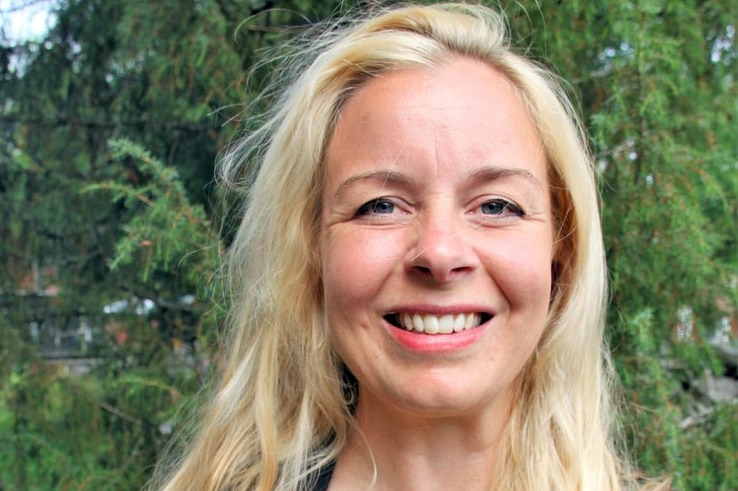 A woman smiles, standing in front of a tree.