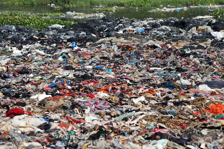 A mountain of clothes dumped by a river.