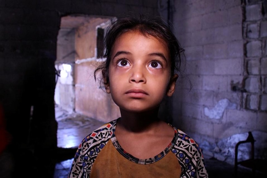 Rula Mosabeh, aged six, stares up at the camera as she stands in her rundown home.