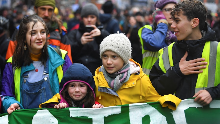Greta Thunberg comforts a crying girl has they march behind a large banner during a climate protest.