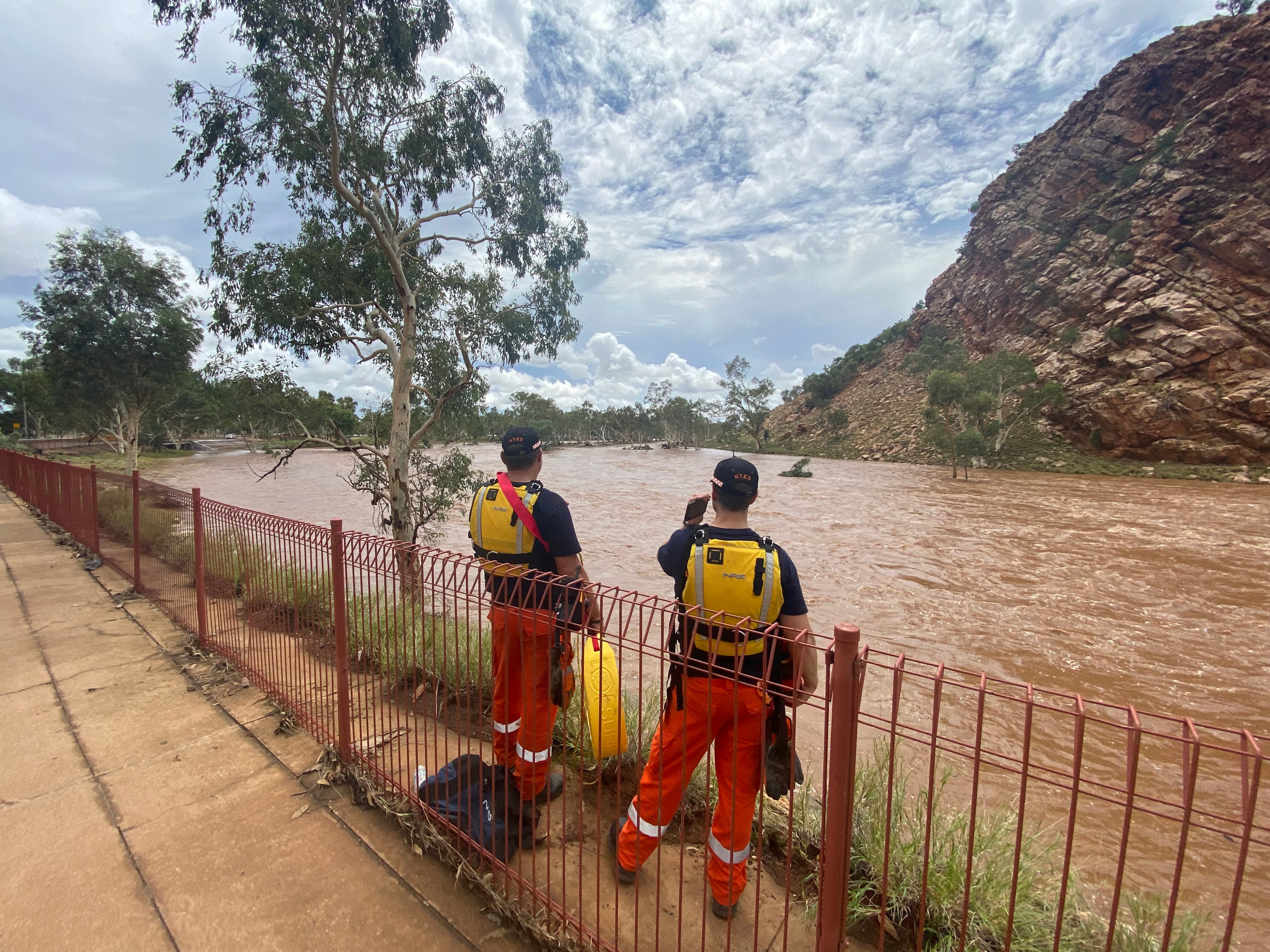 Two people with emergency worker uniforms standing on the side of a river almost bursting at banks