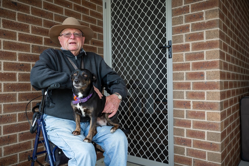 A man sits in front of a home with a dog
