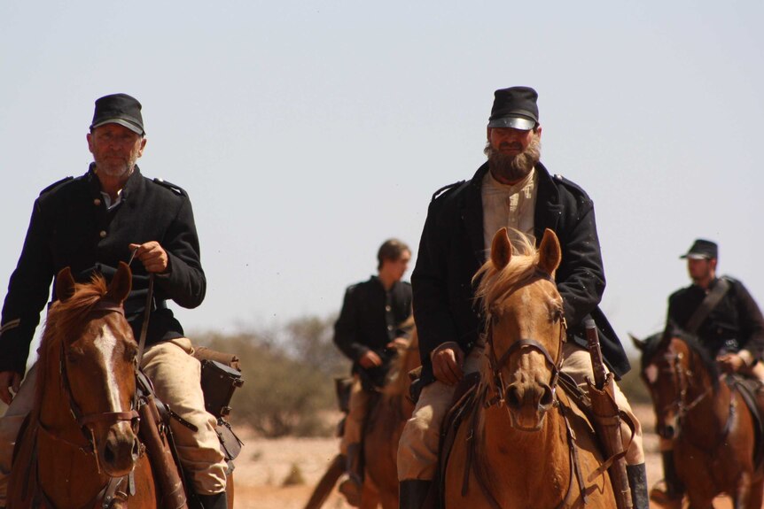 A group of men ride horses wearing heavy black coats and black hats