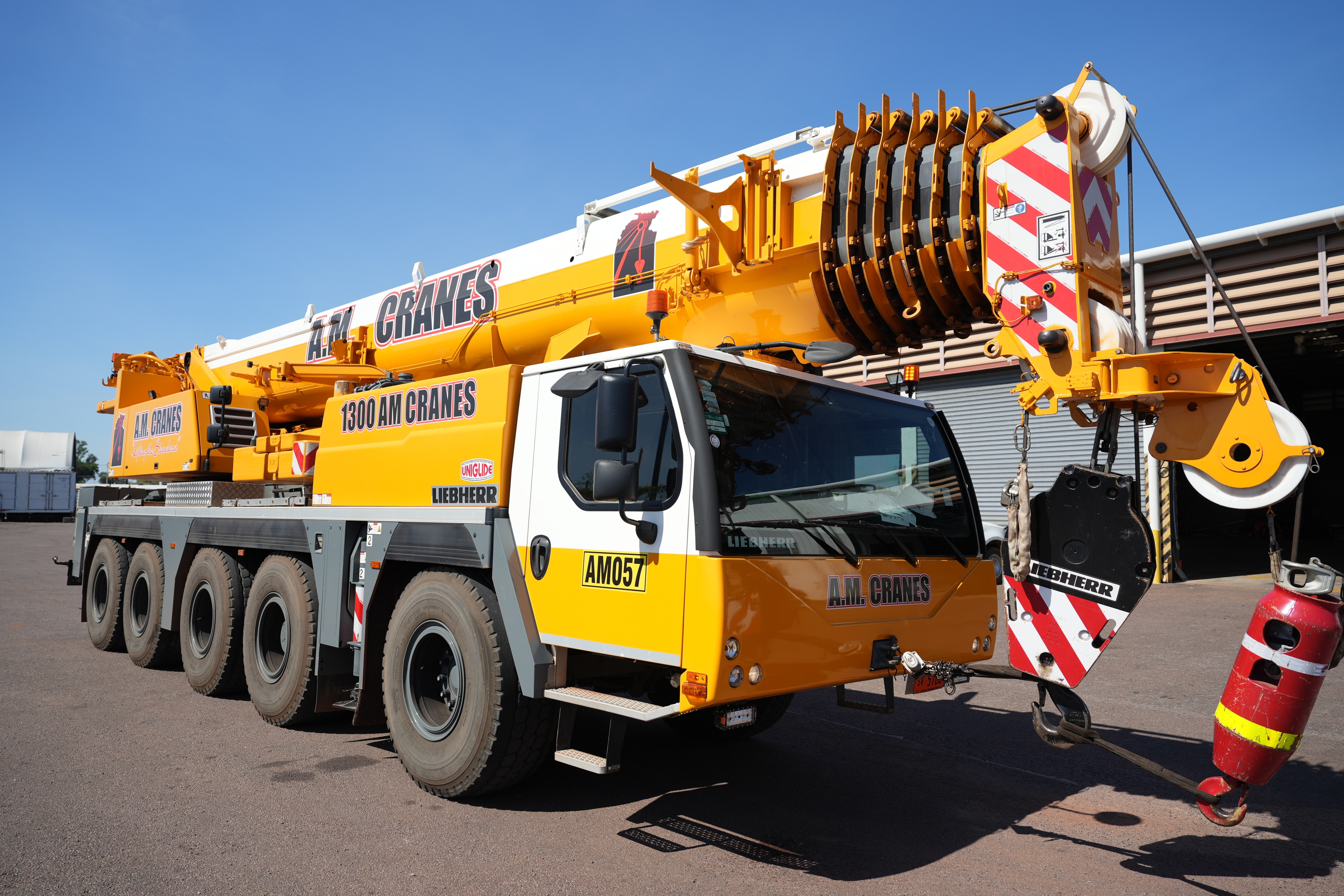 A large yellow crane, parked in an open lot, branded with the words 'A.M. Cranes'.