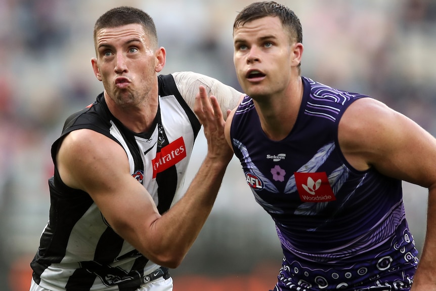 Two male AFL footballers stand shoulder to shoulder while looking at the camera.