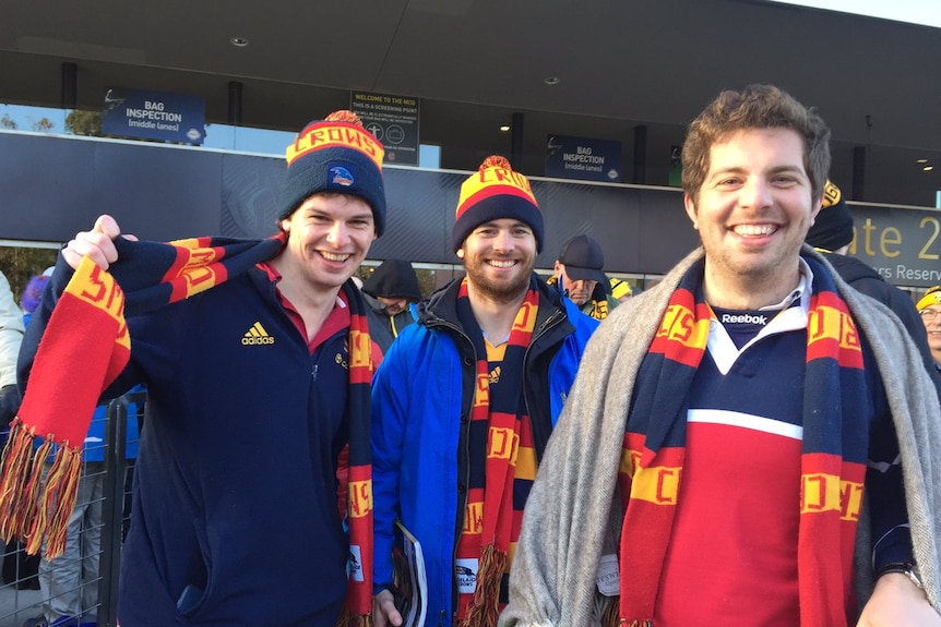 Adelaide supporter Ben waves his Crows scarf, alongside two friends wearing Crows colours.