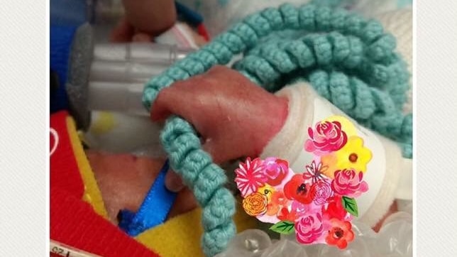A tiny premature baby's hand holding a crochet octopus tentacle