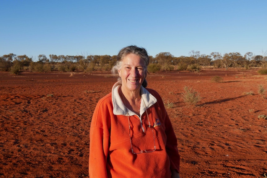 A woman in an orange jumper with red dirt in the background.