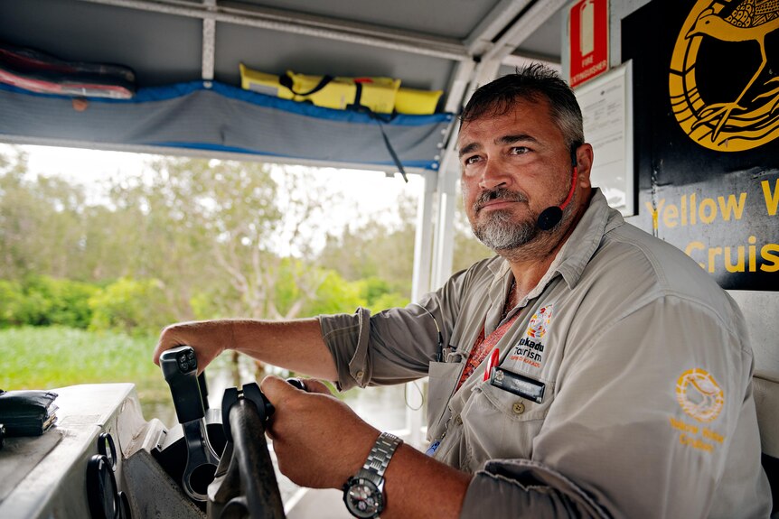 A man driving a boat looks out over the river, looking out past the camera