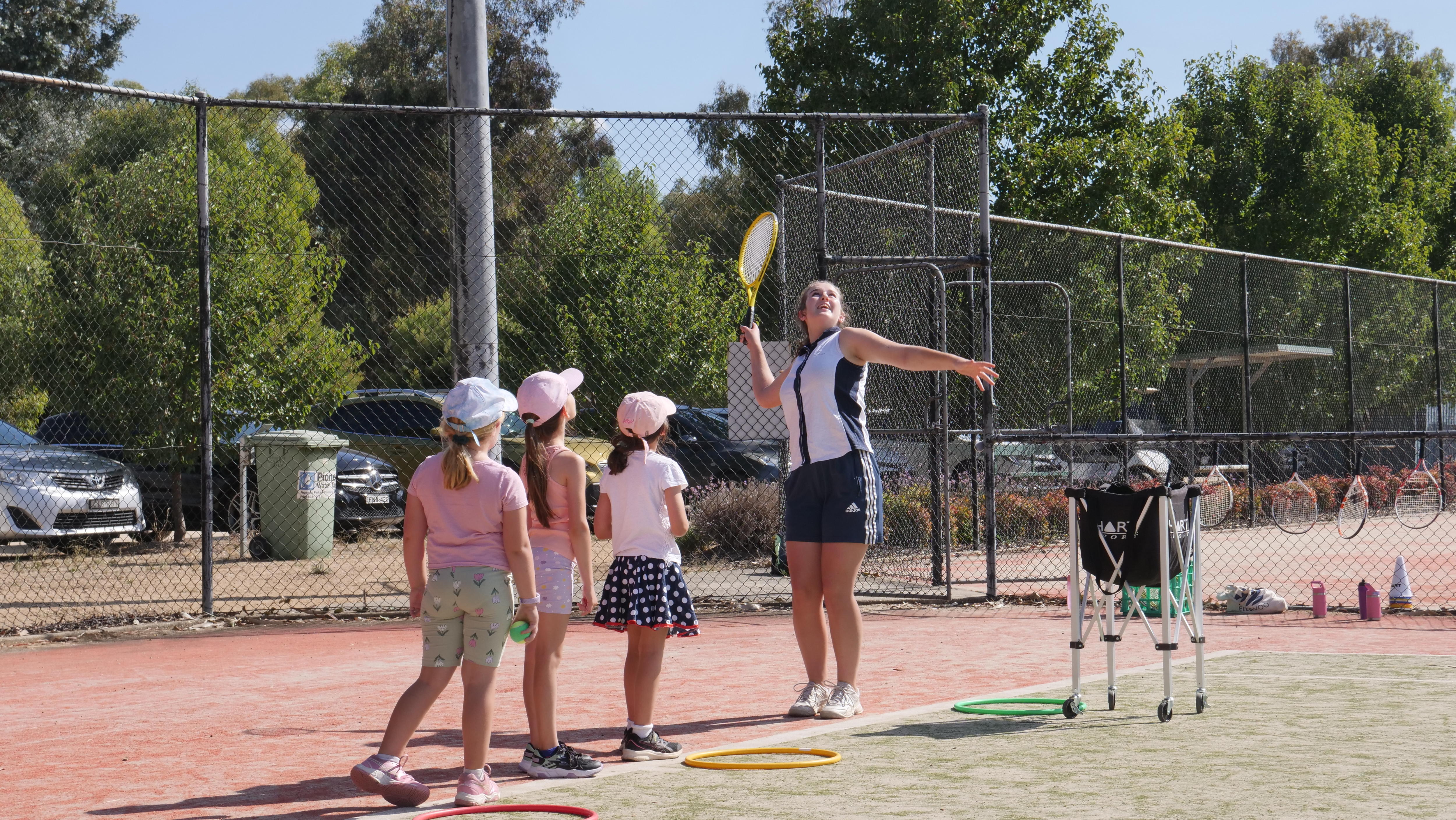 A teenage girl watches a tennis serve she made while several young children look on