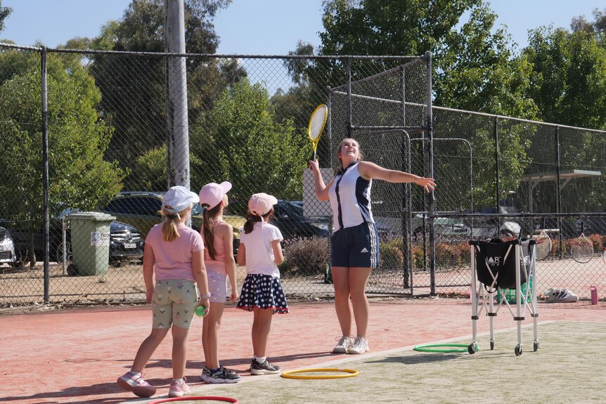 A teenage girl looks up at a tennis serve she has made while several young kids watch