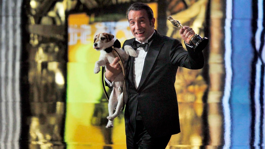 Jean Dujardin carries Uggie the dog after The Artist won the Best Picture Oscar