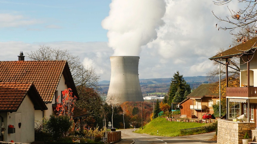 Steam emerges from a cooling tower of a nuclear power plant in the background of a Swiss street.