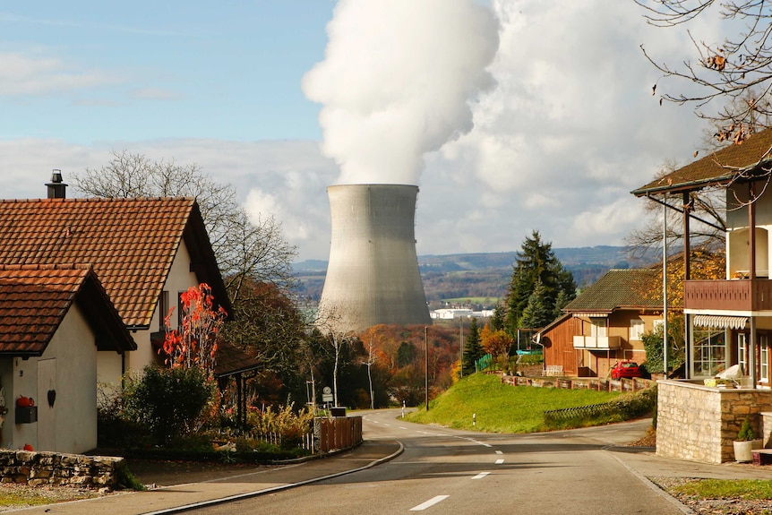 Steam emerges from a cooling tower of a nuclear power plant in the background of a Swiss street.