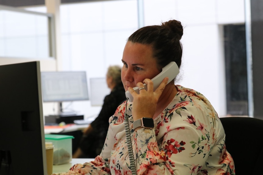 A woman sits at a desk, talking on the phone.