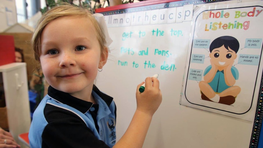 A young school student draws on a whiteboard.