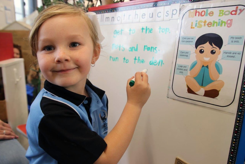 A young school student draws on a whiteboard.