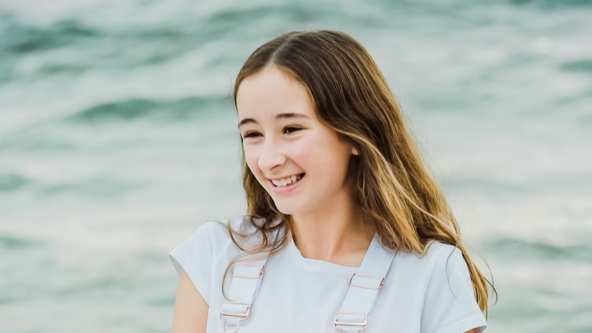 A portrait of Amber Jess Millar smiling and standing in front of the ocean 