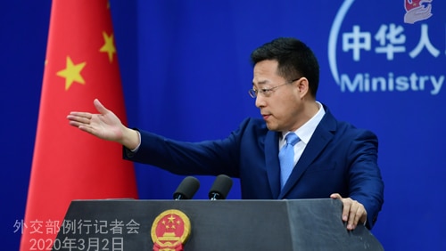 A man gestures with his hand standing in front of a Chinese flag standing in front of a podium.