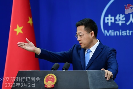 A man gestures with his hand standing in front of a Chinese flag standing in front of a podium.