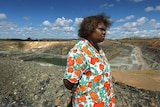 An Indigenous woman in a bright top stands in front of a vast mine.
