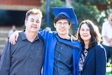 A young man in a blue graduation gown and cap with his father on the left and mother on the right.
