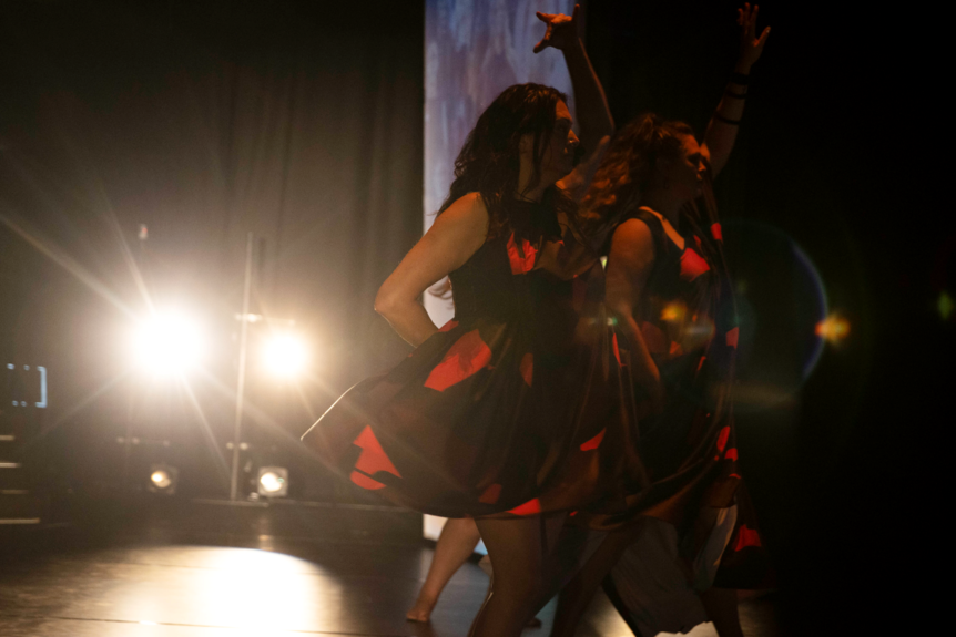 A group of dancers moves around a stage with a light shining in the background