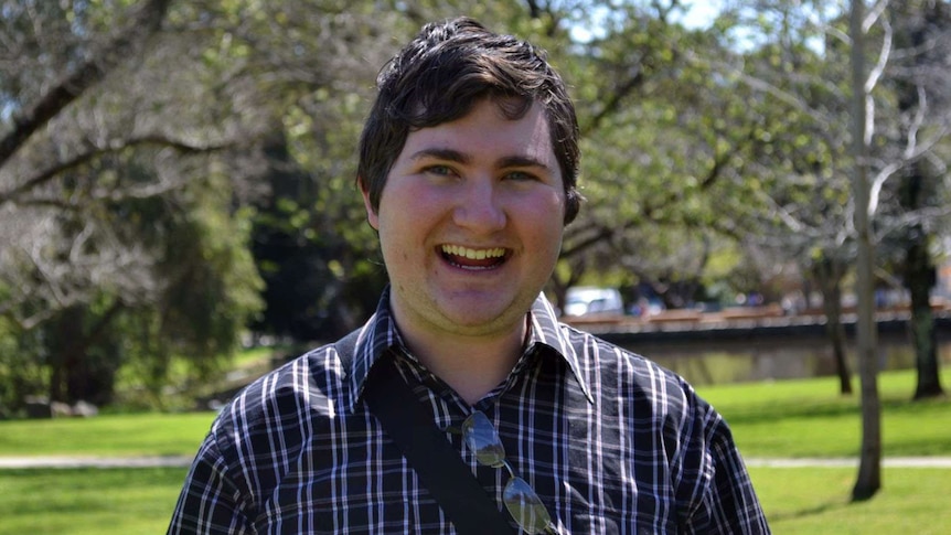 A smiling Joshua Fisher-Turner in headshot with trees in the background.