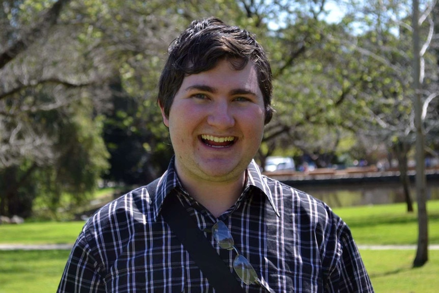 A smiling Joshua Fisher-Turner in headshot with trees in the background.