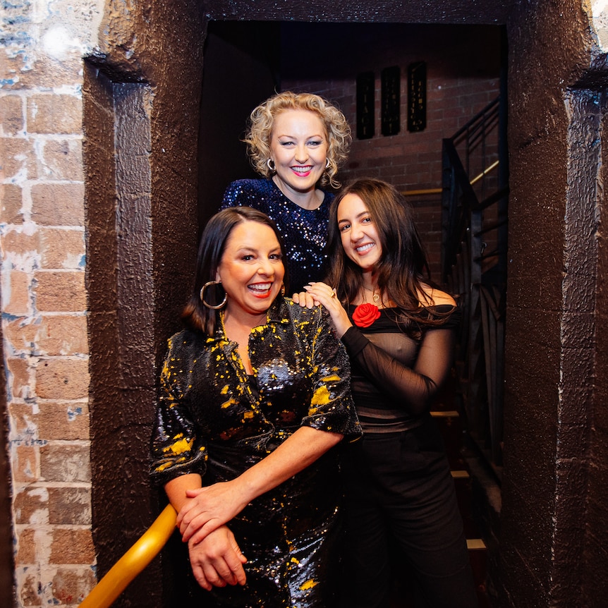 Myf, Zan and Concetta Caristo standing in an exposed brick doorway smiling together