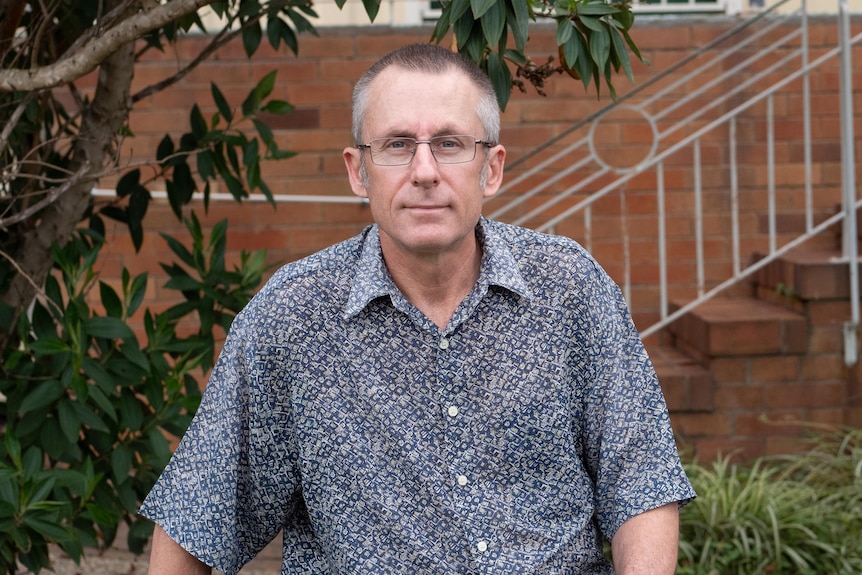 A man sits on the brick wall outside a red brick house.