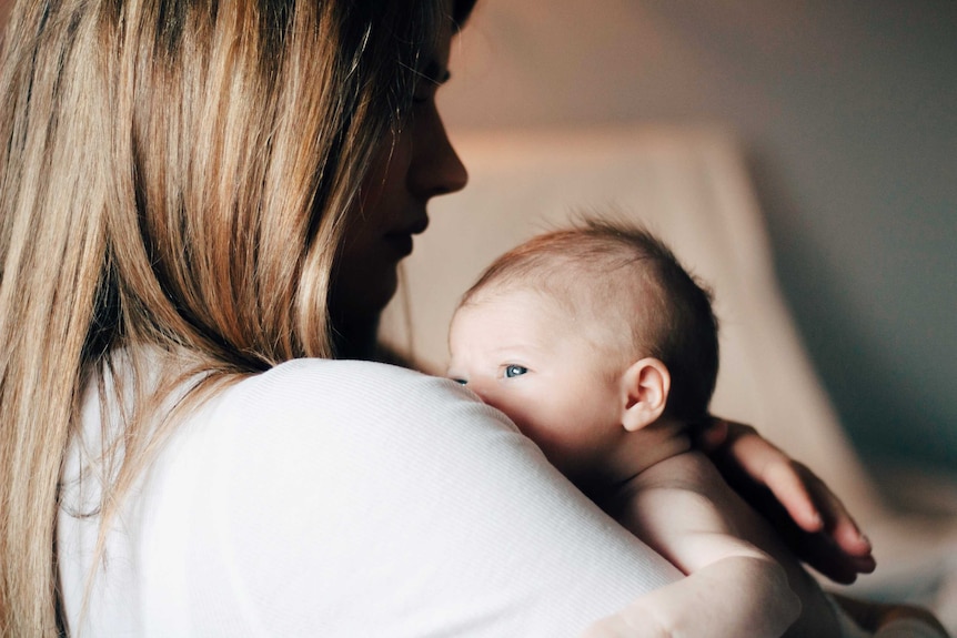 A newborn baby peeps over a woman's shoulder.