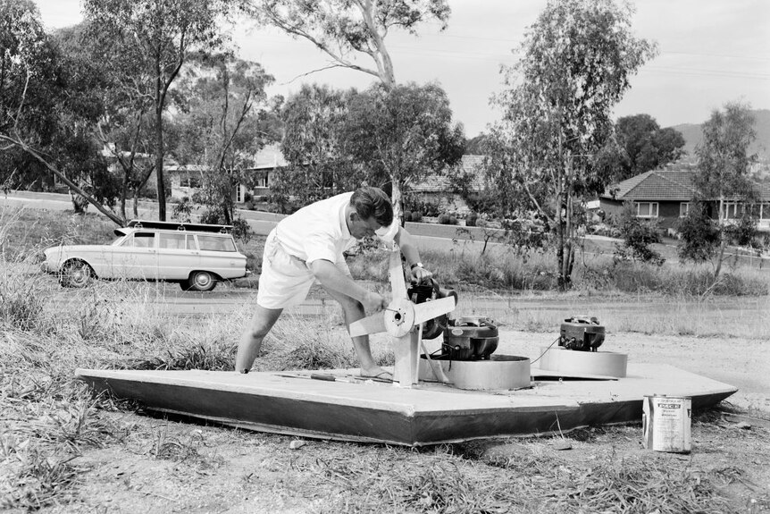 A black and white photo of a man building a hovercraft.
