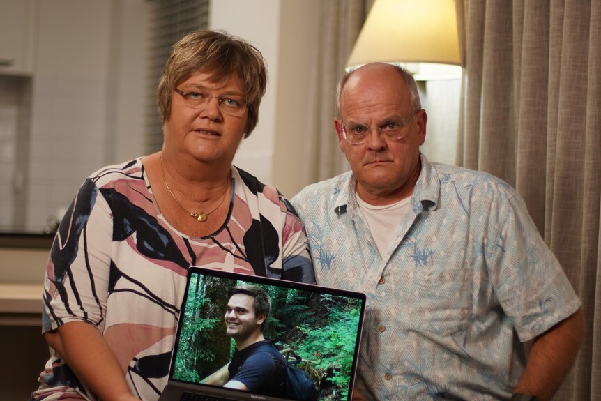A couple hold a laptop look serious as they show an image of their son on a laptop screen.