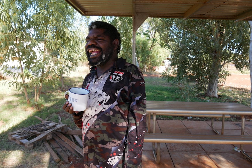 A man laughs as he holds a drinking mug.