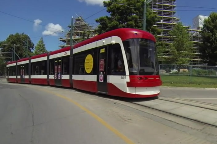 A red streetcar tram travelling along in the city of Toronto