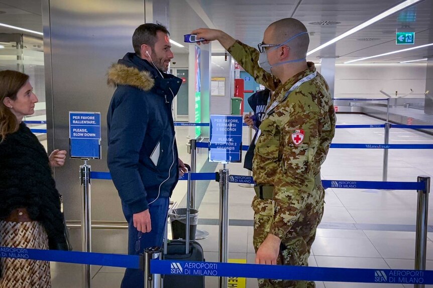 A man in military fatigues takes the temperature of an airline passenger in an airport.