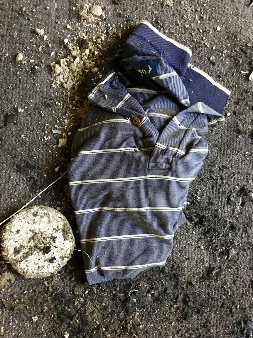 A blue and shite striped shirt lies on the ground surrounded by debris after a house fire.