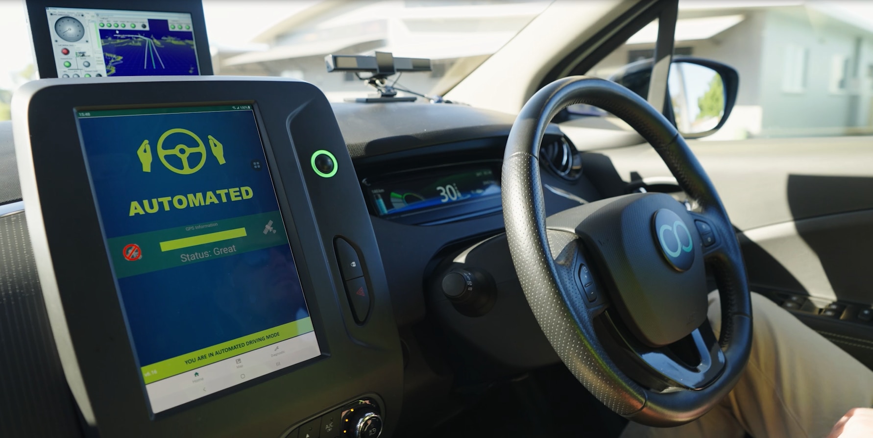 Inside a small vehicle showing a black dashboard with small computer screen and a steering wheel