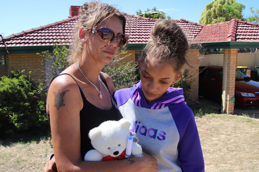 Denishar Woods' mother Lacey Harrison and sister Anita Woods stand outside their Beldon home holding a white teddy bear.