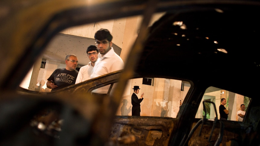 Israelis are seen through a burned car after a rocket fired from Gaza landed in Ashdod October 29, 2011