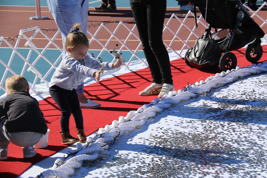 Toddler throwing a handful of coins into giant heart for cancer charity