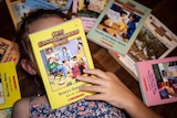 Girl holds Babysitters Club book in front of her face for story on watching remakes in coronavirus isolation