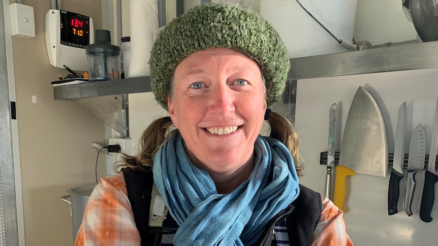 Female farmer in a hat and apron stands with folded arms in a workspace.