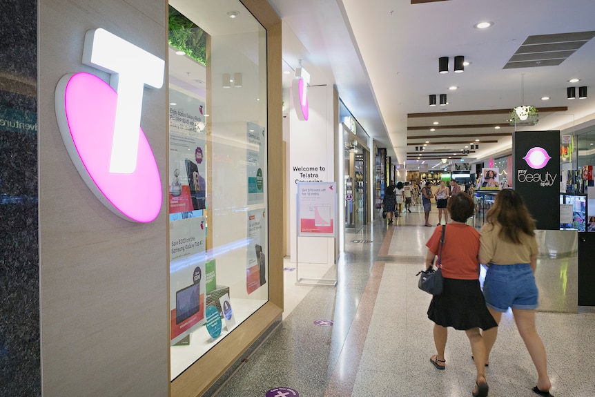 A Telstra sign outside a store in a mall.
