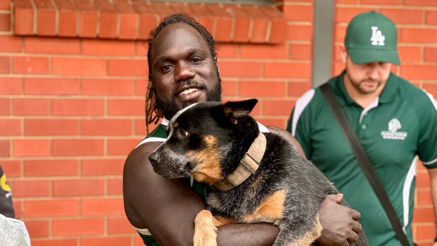Footy player smiles at camera, holding his dog