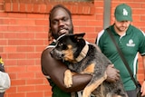 Footy player smiles at camera, holding his dog